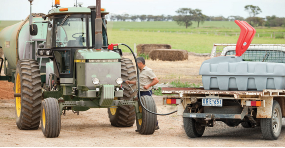 Tractor connected to a trailer with a person on a dirt road in a rural setting.